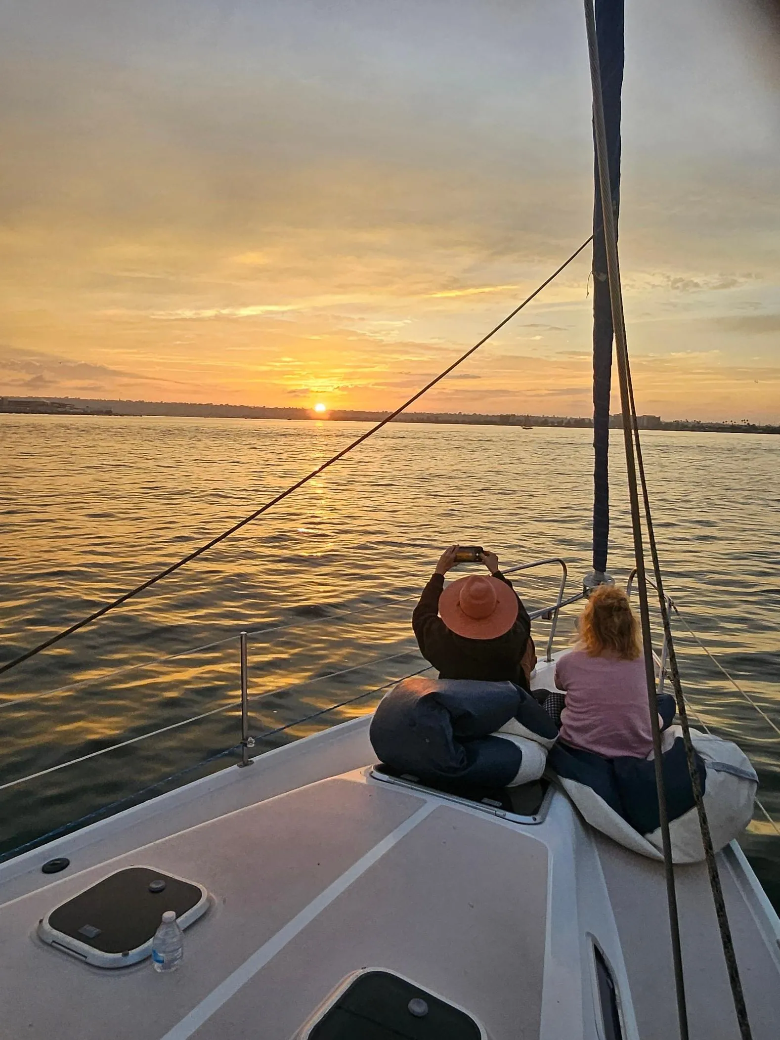 The bow of a sailboat pointing at the sunset on San Diego Bay