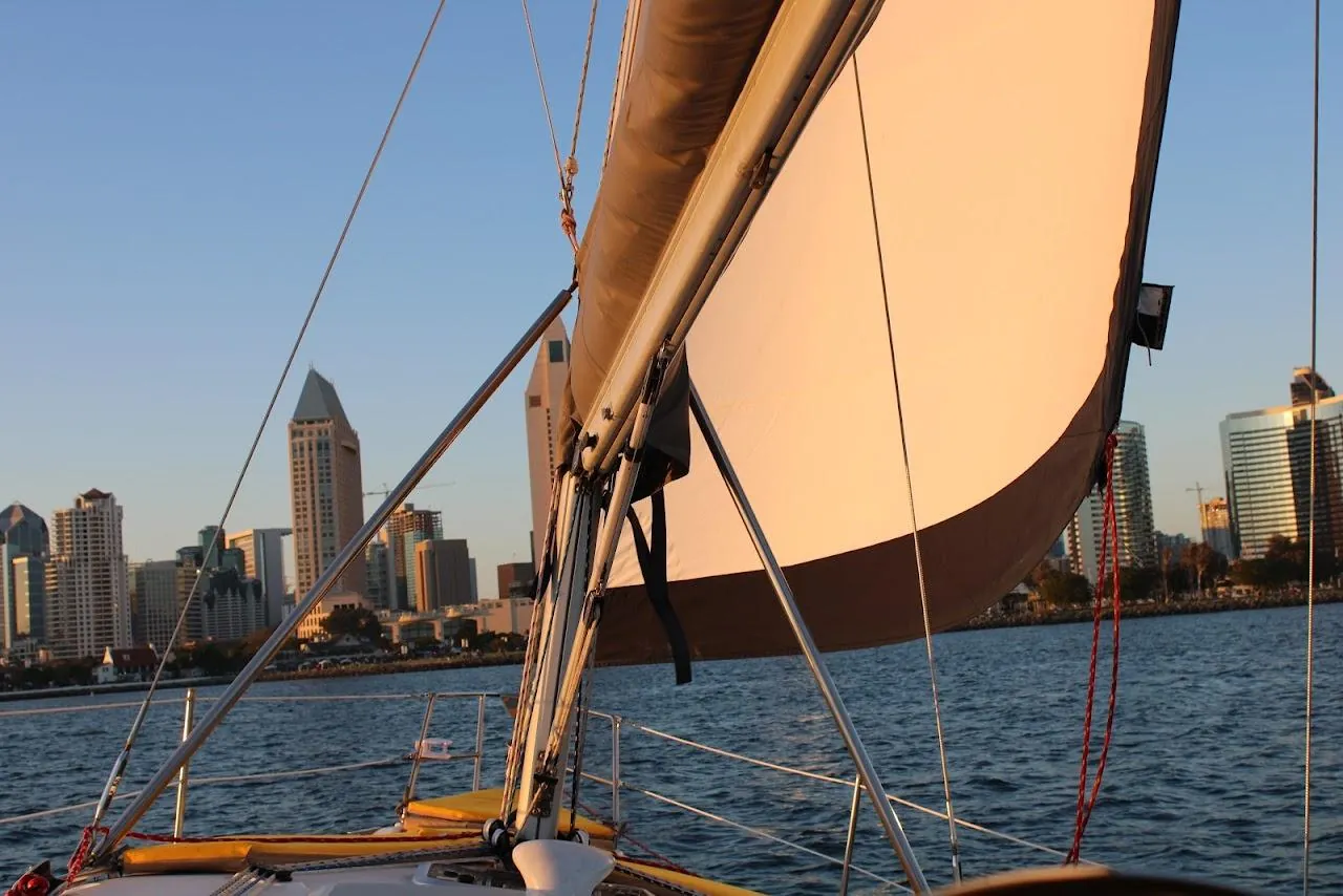 A sailboat's sail and the San Diego skyline at sunset